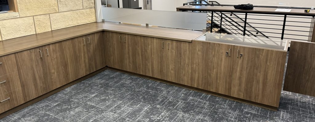 L-shaped walnut-finish base cabinets and countertop with frosted glass privacy screen, beside an office stair railing
