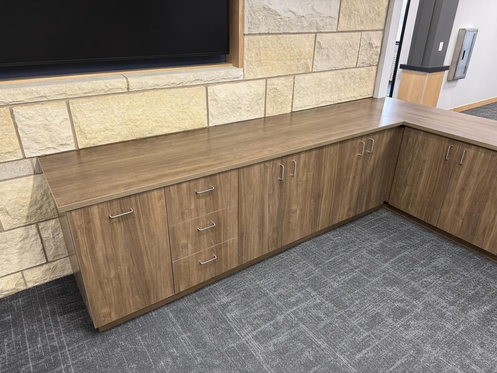 Walnut-finish L-shaped base cabinets with matching top, wire pulls and a three-drawer stack below a stone accent wall