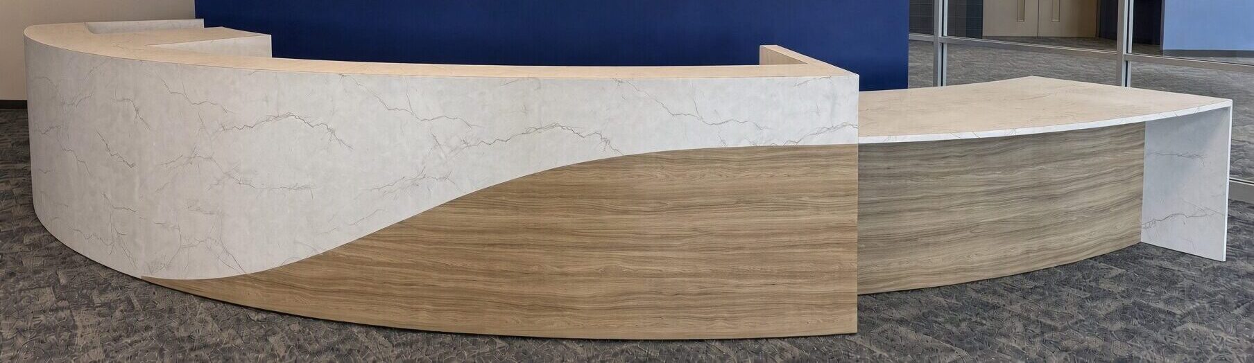 Curved reception desk with white veined stone-look front, sweeping wood-grain wave panel and attached work counter