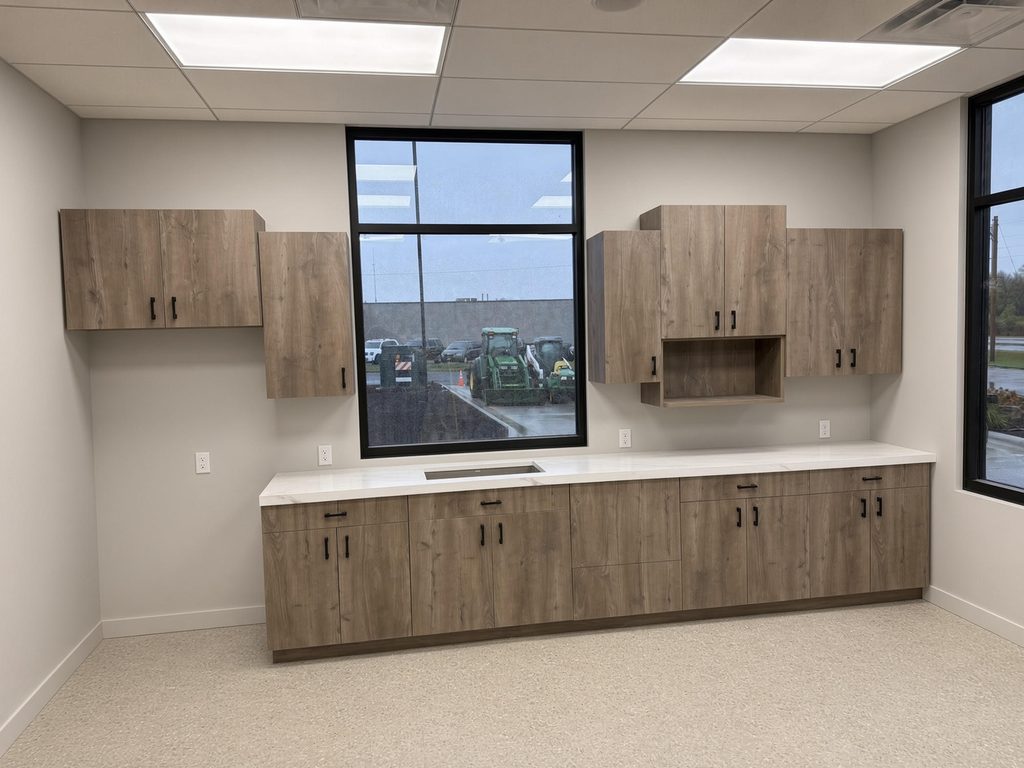 Break room casework with oak-look upper and lower cabinets, black pulls, white stone-look counter and sink