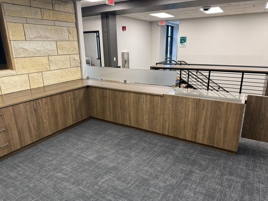 Walnut-finish L-shaped counter with frosted glass privacy panel and glass-top display cabinet in an open lobby