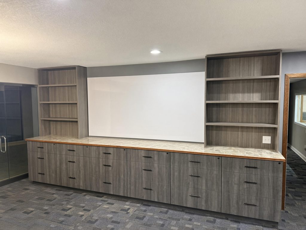 Gray wood-look wall of file drawers with open bookcases flanking a whiteboard, topped by a stone-look counter with wood edge