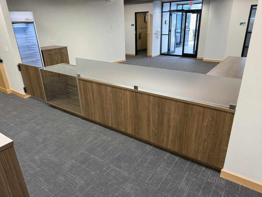 Walnut-finish service counter with frosted glass transaction screen and glass display case, seen from the lobby side