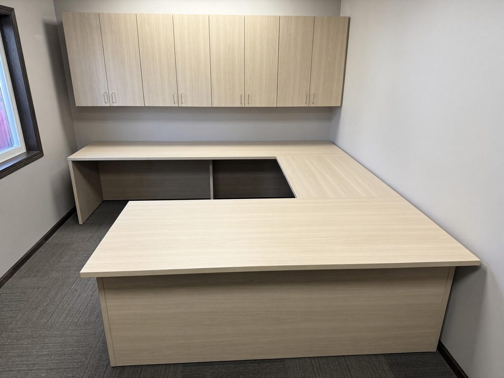 U-shaped desk in light oak-look finish with a row of matching wall-mounted storage cabinets in a private office